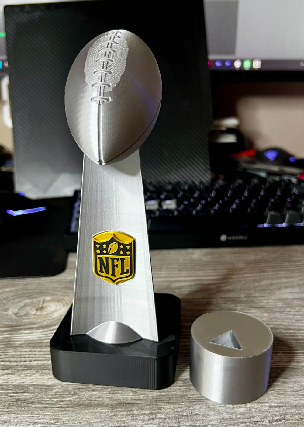 The printed Super Bowl trophy in silver on its black base, the round hand adapter beside it